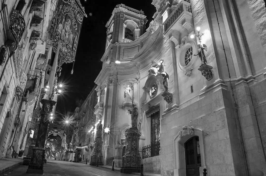 St Dominic’s Basilica illuminated at night above decorated festa streets.