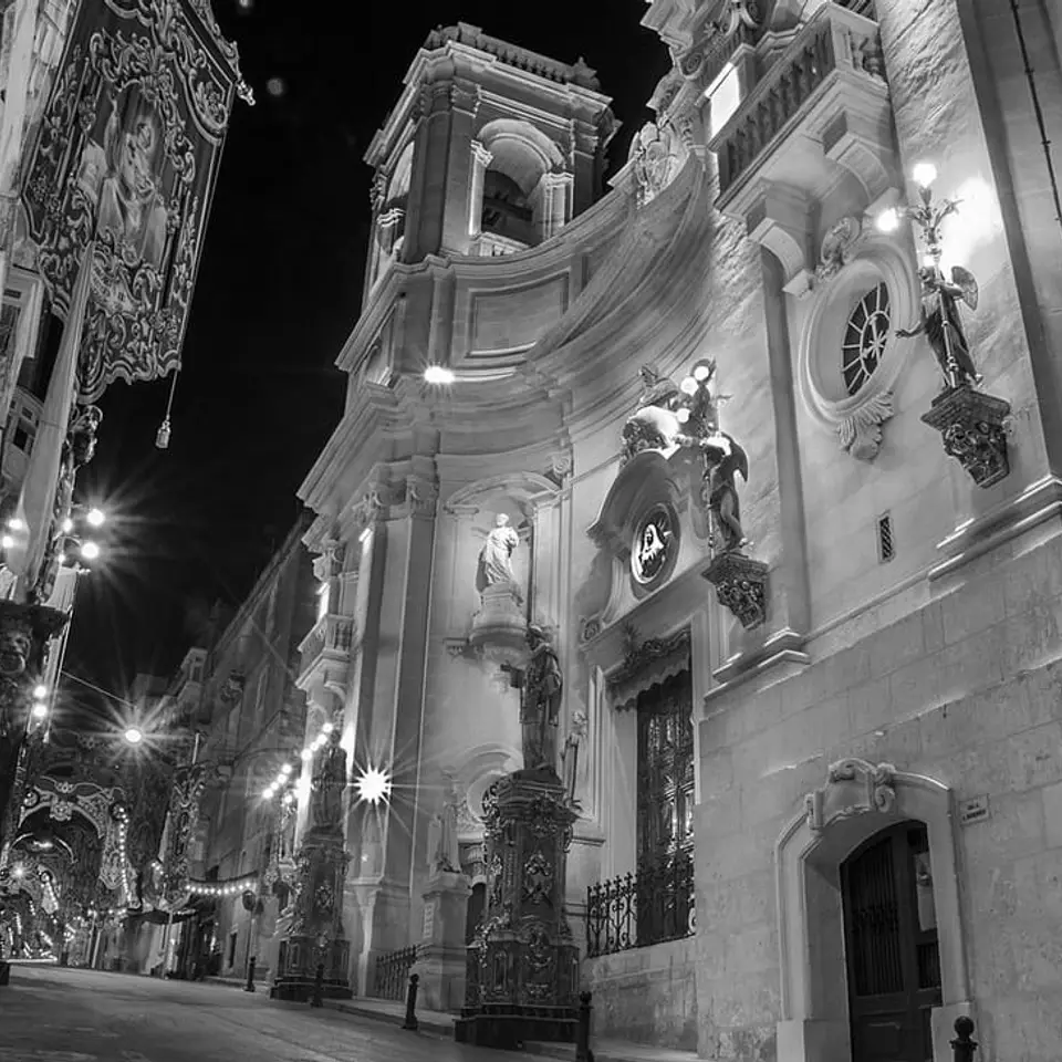 St Dominic’s Basilica illuminated at night above decorated festa streets.